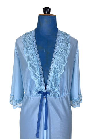 Vintage 1970s negligee robe in sky blue with wide lace trim along the deep V neckline and three-quarter length sleeve cuffs. Finished with a decorative royal blue bow. Closes at the waist with a single button.