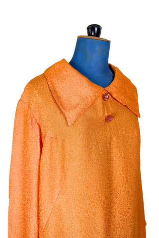 Vintage 1960s orange textured mod dress with long sleeves, large pointed collar, and two decorative rhinestone buttons. The long sleeves have turned cuffs. The A-line dress has bust darts through the sides and diagonally down towards the hips. Closes in the back with a cotton twill zipper.