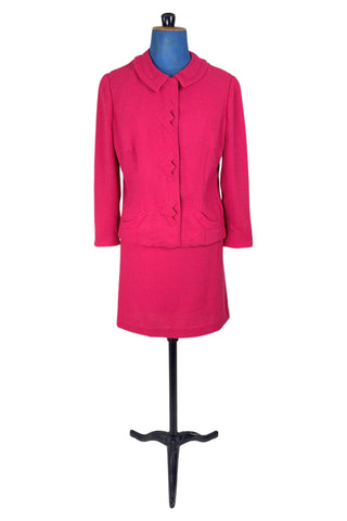 Vintage early 1960s skirt suit with matching jacket and pencil skirt in hot pink medium-weight wool crepe. The jacket features a small round collar, rounded pockets and zigzag appliqué button covers. The skirt has small pleats in the front and darts in the back to add shape. The suit is fully lined in pink rayon crepe.