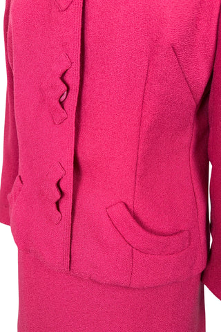 Vintage early 1960s skirt suit with matching jacket and pencil skirt in hot pink medium-weight wool crepe. The jacket features a small round collar, rounded pockets and zigzag appliqué button covers. The skirt has small pleats in the front and darts in the back to add shape. The suit is fully lined in pink rayon crepe.