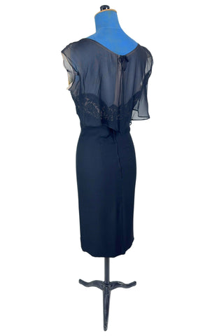 Vintage 1950s black chiffon cocktail dress with strapless lace bodice with chiffon overlay, finished with a empire waist sash with bow. The top of the bodice has a light beige chiffon layer creating a nude illusion, with a floating outer layer of black chiffon that continues in the back as a waist-length cape. A tiny bow perfectly sets off the back of the collar. 

The dress closes in the back with a metal zipper, and is fully lined. 

In excellent vintage condition, with minor wear to the chiffon near...