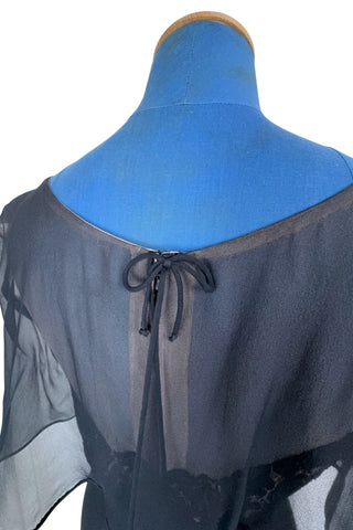 Vintage 1950s black chiffon cocktail dress with strapless lace bodice with chiffon overlay, finished with a empire waist sash with bow. The top of the bodice has a light beige chiffon layer creating a nude illusion, with a floating outer layer of black chiffon that continues in the back as a waist-length cape. A tiny bow perfectly sets off the back of the collar. 

The dress closes in the back with a metal zipper, and is fully lined. 

In excellent vintage condition, with minor wear to the chiffon near...