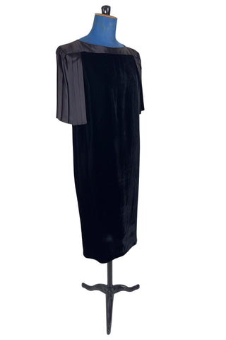 Vintage 1980s cocktail dress in black velvet with pleated black satin sleeves. The dress has a straight column silhouette. The back features a deep V pleated satin panel and satin strap across the back with small buttons at the back of the collar. The dress has no zipper or other closure.

Designed by Lady Kate. Union made in U.S.A. by ILGWU / AFL CIO. Marked Size 8 Petite.