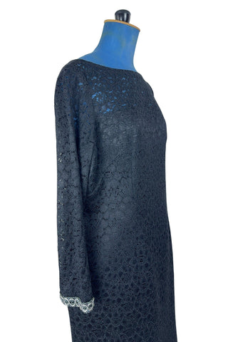Vintage 1960s cocktail dress in black corded lace with see-through upper bodice and sleeves. The long sleeves are embellished with silver corded soutache trim. The dress closes in the back with a cotton twill zipper, and is fully lined.