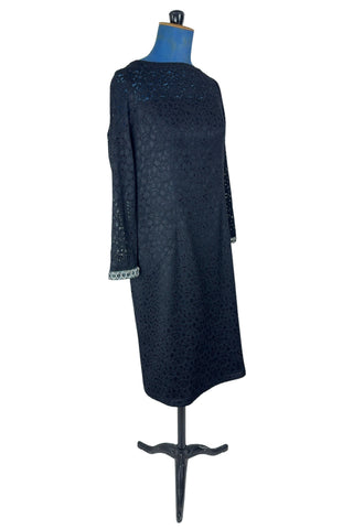 Vintage 1960s cocktail dress in black corded lace with see-through upper bodice and sleeves. The long sleeves are embellished with silver corded soutache trim. The dress closes in the back with a cotton twill zipper, and is fully lined.