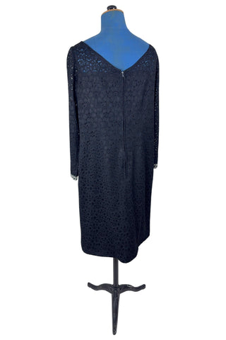 Vintage 1960s cocktail dress in black corded lace with see-through upper bodice and sleeves. The long sleeves are embellished with silver corded soutache trim. The dress closes in the back with a cotton twill zipper, and is fully lined.
