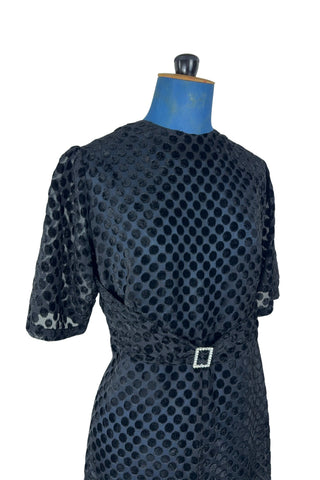 Vintage 1960s sheer black dress with flocked polkadot design. This sweet little black dress features short sleeves, and an integrated sash belt across the front with a rhinestone buckle belt. The dress closes in the back with a cotton twill zipper and is unlined. 