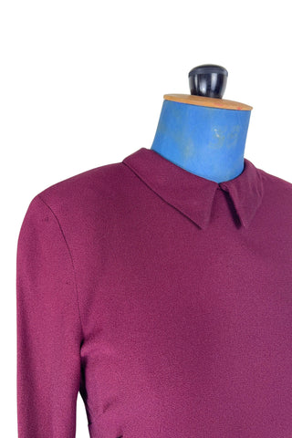 Vintage 1930s day dress in burgundy wool crepe, featuring a small pointed collar, long sleeves with turned cuffs, and three wide bias-cut tucks at the hip forming a peplum flounce around the front. In the back, the peplum becomes a waterfall pleat panel down the middle back. The dress closes in the back with a metal zipper, and is unlined. 