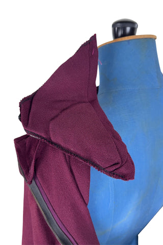 Vintage 1930s day dress in burgundy wool crepe, featuring a small pointed collar, long sleeves with turned cuffs, and three wide bias-cut tucks at the hip forming a peplum flounce around the front. In the back, the peplum becomes a waterfall pleat panel down the middle back. The dress closes in the back with a metal zipper, and is unlined. 