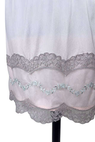 Vintage 1950s Kayser half slip in light pink with grey scalloped lace trim. The bottom of the slip is decorated with a wide panel of overlay chiffon embroidered with a floral chain. The waist is elasticized.

Designed by Kayser. Made in Canada. Marked size Small / Short.