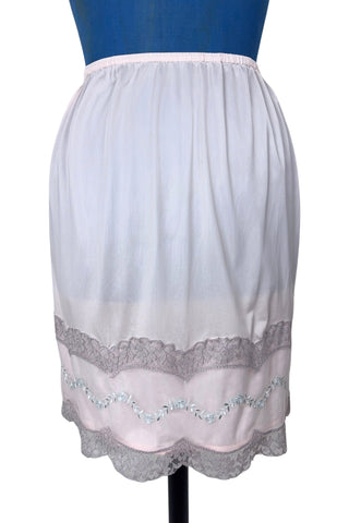 Vintage 1950s Kayser half slip in light pink with grey scalloped lace trim. The bottom of the slip is decorated with a wide panel of overlay chiffon embroidered with a floral chain. The waist is elasticized.

Designed by Kayser. Made in Canada. Marked size Small / Short.
