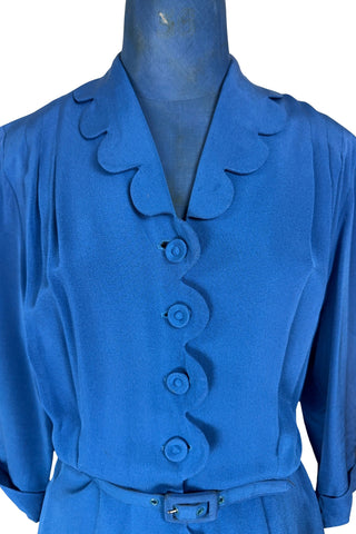 Vintage 1940s day dress in royal blue rayon with scalloped collar and front button placket, which closes with 14 functional self-fabric buttons down the front. The dress has three quarter sleeves with folded cuffs, and a matching self-fabric belt with a rectangular covered buckle. 
Condition Note: The dress is in very good vintage condition, with an inconspicuous small darkened area on the lower back of the skirt about 1-2” long.