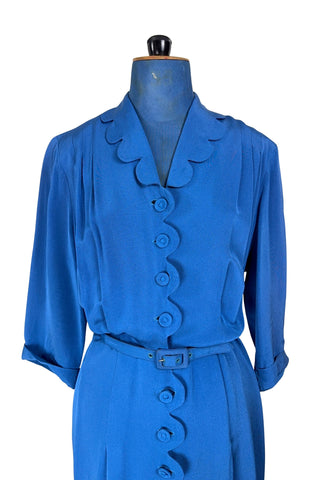 Vintage 1940s day dress in royal blue rayon with scalloped collar and front button placket, which closes with 14 functional self-fabric buttons down the front. The dress has three quarter sleeves with folded cuffs, and a matching self-fabric belt with a rectangular covered buckle. 
Condition Note: The dress is in very good vintage condition, with an inconspicuous small darkened area on the lower back of the skirt about 1-2” long.