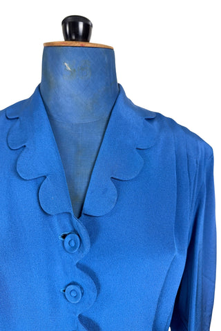 Vintage 1940s day dress in royal blue rayon with scalloped collar and front button placket, which closes with 14 functional self-fabric buttons down the front. The dress has three quarter sleeves with folded cuffs, and a matching self-fabric belt with a rectangular covered buckle. 
Condition Note: The dress is in very good vintage condition, with an inconspicuous small darkened area on the lower back of the skirt about 1-2” long.