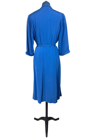 Vintage 1940s day dress in royal blue rayon with scalloped collar and front button placket, which closes with 14 functional self-fabric buttons down the front. The dress has three quarter sleeves with folded cuffs, and a matching self-fabric belt with a rectangular covered buckle. 
Condition Note: The dress is in very good vintage condition, with an inconspicuous small darkened area on the lower back of the skirt about 1-2” long.