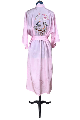 Vintage 1960s kimono style robe in light pink rayon damask, with embroidered crane birds and nature scenes. Features a deep V neckline, three-quarter length wide sleeves, and two large pockets decorated with embroidery. The back of the robe has a large embroidered motif.
