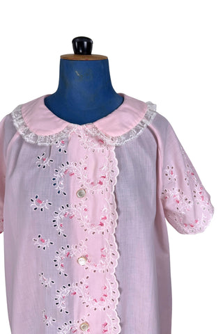 Vintage late 1950s robe in light pink with large scalloped eyelet embroidery down the front and around the short sleeves. The peignoir style robe features short sleeves with matching openwork floral embroidery, and a Peter Pan collar trimmed with dainty white lace. The robe closes with five flat ivory pearl buttons, and a hidden snap under the collar.

A Perri-Ann design by Faris. Made in Canada.