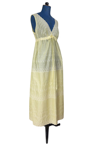Vintage 1960s nightgown in yellow cotton with white eyelet embroidery. The nightgown is sleeveless, with a deep V neckline and gathered empire waist which ties with a yellow ribbon woven through eyelet lace trim. The back of the nightgown has a similar deep V cut.