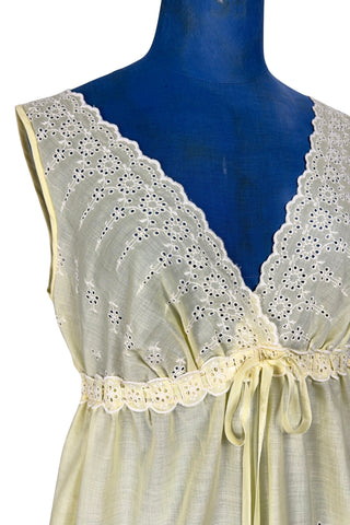 Vintage 1960s nightgown in yellow cotton with white eyelet embroidery. The nightgown is sleeveless, with a deep V neckline and gathered empire waist which ties with a yellow ribbon woven through eyelet lace trim. The back of the nightgown has a similar deep V cut.