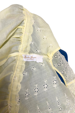 Vintage 1960s nightgown in yellow cotton with white eyelet embroidery. The nightgown is sleeveless, with a deep V neckline and gathered empire waist which ties with a yellow ribbon woven through eyelet lace trim. The back of the nightgown has a similar deep V cut.