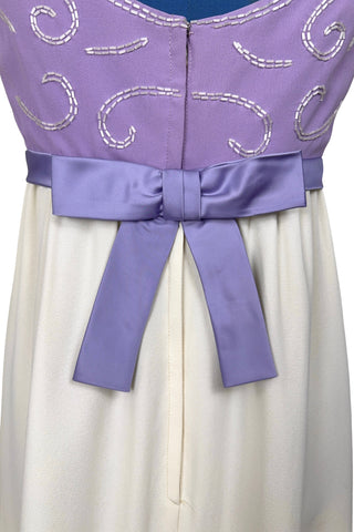 Gorgeous vintage 1960s evening gown with lilac purple bodice and creamy white long A-line skirt. The empire waist gown’s bodice features swirls of pearly white beading, and is finished with a wide purple satin sash at the waist with a large bow in the back.

The sleeveless dress has a wide round collar with a lower scoop back. It is fully lined, and closes in the back with a cotton twill nylon zipper.