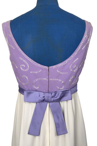 Gorgeous vintage 1960s evening gown with lilac purple bodice and creamy white long A-line skirt. The empire waist gown’s bodice features swirls of pearly white beading, and is finished with a wide purple satin sash at the waist with a large bow in the back.

The sleeveless dress has a wide round collar with a lower scoop back. It is fully lined, and closes in the back with a cotton twill nylon zipper.