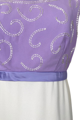 Gorgeous vintage 1960s evening gown with lilac purple bodice and creamy white long A-line skirt. The empire waist gown’s bodice features swirls of pearly white beading, and is finished with a wide purple satin sash at the waist with a large bow in the back.

The sleeveless dress has a wide round collar with a lower scoop back. It is fully lined, and closes in the back with a cotton twill nylon zipper.