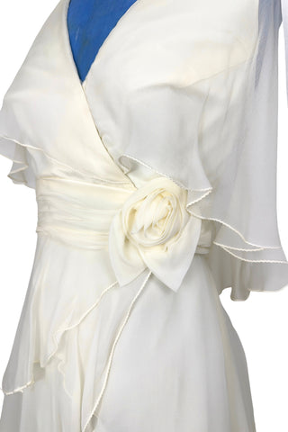 Delicate and lovely 1970s gown in layered cream white silk chiffon. This heavenly dress is composed of layers of cream silk chiffon in an Edwardian-inspired column silhouette. Featuring a deep V halter neckline, the bodice has a built-in cape of sheer chiffon which covers the shoulders and back to the waist. A gathered sash of chiffon is set-off with a large rosette to one side. The sash fastens inconspicuously under the flower so that the fasteners are hidden. The back of the neck has different loop...