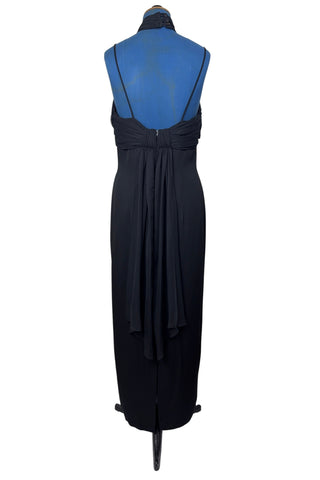 Vintage 1990s black evening gown with silver tone rhinestone brooch at the neck. This sophisticated dress has a column silhouette, and features a sweetheart neckline, spaghetti straps, and a slit at the back of the skirt. Sheer black chiffon is layered and draped at the neck in a halter style, and flows down the bodice to the back of the waist where it forms a floating overlay ruffle.

The dress is fully lined with black acetate, and closes in the back with a nylon zipper.

Marked Size 10. Made in U.S.A.