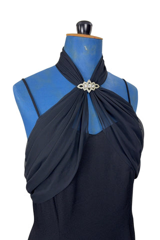 Vintage 1990s black evening gown with silver tone rhinestone brooch at the neck. This sophisticated dress has a column silhouette, and features a sweetheart neckline, spaghetti straps, and a slit at the back of the skirt. Sheer black chiffon is layered and draped at the neck in a halter style, and flows down the bodice to the back of the waist where it forms a floating overlay ruffle.

The dress is fully lined with black acetate, and closes in the back with a nylon zipper.

Marked Size 10. Made in U.S.A.
