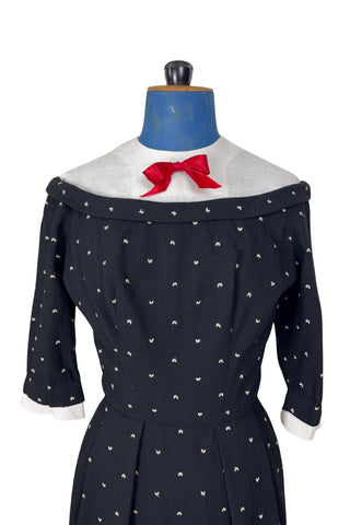 Unique true vintage 1950s “secretary” dress with detachable collar and cuffs for easy washing and ironing. The dress is made of black cotton (may have some linen content as well) with tiny white arc shaped embroidered polkadots. The collar and cuffs are made of crisp white linen/cotton, and attach with a series of metal snaps around the neckline and cuffs. The collar has a set of two bound buttonholes that a ribbon or scarf may be threaded through. The dress can be worn with any combination of collar,...