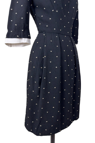 Unique true vintage 1950s “secretary” dress with detachable collar and cuffs for easy washing and ironing. The dress is made of black cotton (may have some linen content as well) with tiny white arc shaped embroidered polkadots. The collar and cuffs are made of crisp white linen/cotton, and attach with a series of metal snaps around the neckline and cuffs. The collar has a set of two bound buttonholes that a ribbon or scarf may be threaded through. The dress can be worn with any combination of collar,...