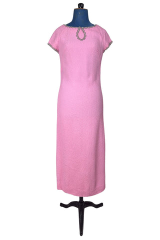 Stunning true vintage 1960s evening gown in candy pink textured crepe with scalloped silver beading at the neckline and trimming the short sleeve cuffs.

The gown is designed with a close-fitting column silhouette, while the textured crepe molds beautifully to your curves.

The gown is fully lined and closes in the back with a cotton twill nylon zipper.