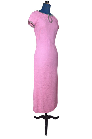 Stunning true vintage 1960s evening gown in candy pink textured crepe with scalloped silver beading at the neckline and trimming the short sleeve cuffs.

The gown is designed with a close-fitting column silhouette, while the textured crepe molds beautifully to your curves.

The gown is fully lined and closes in the back with a cotton twill nylon zipper.
