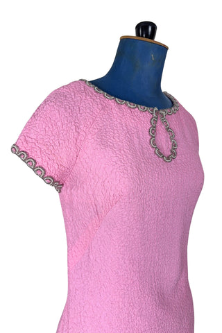 Stunning true vintage 1960s evening gown in candy pink textured crepe with scalloped silver beading at the neckline and trimming the short sleeve cuffs.

The gown is designed with a close-fitting column silhouette, while the textured crepe molds beautifully to your curves.

The gown is fully lined and closes in the back with a cotton twill nylon zipper.