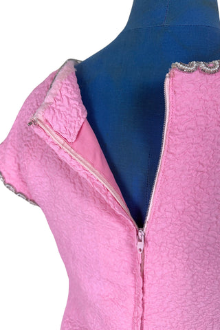 Stunning true vintage 1960s evening gown in candy pink textured crepe with scalloped silver beading at the neckline and trimming the short sleeve cuffs.

The gown is designed with a close-fitting column silhouette, while the textured crepe molds beautifully to your curves.

The gown is fully lined and closes in the back with a cotton twill nylon zipper.