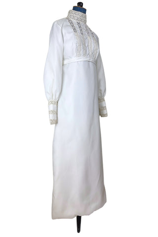 Vintage late 1960s or early 1970s wedding dress with high neck, long sleeves, and an empire waist. This Edwardian revival style dress features crochet lace panels at the neck, down the front and back of the bodice, and trimming the long sleeve cuffs. The dress has a large flat bow at the back of the waist.

Channel your inner Priscilla Presley in this lovely vintage gown.

The dress closes in the back with a cotton twill nylon zipper.