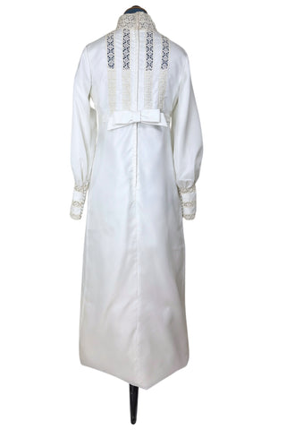 Vintage late 1960s or early 1970s wedding dress with high neck, long sleeves, and an empire waist. This Edwardian revival style dress features crochet lace panels at the neck, down the front and back of the bodice, and trimming the long sleeve cuffs. The dress has a large flat bow at the back of the waist.

Channel your inner Priscilla Presley in this lovely vintage gown.

The dress closes in the back with a cotton twill nylon zipper.