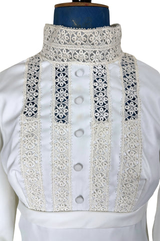 Vintage late 1960s or early 1970s wedding dress with high neck, long sleeves, and an empire waist. This Edwardian revival style dress features crochet lace panels at the neck, down the front and back of the bodice, and trimming the long sleeve cuffs. The dress has a large flat bow at the back of the waist.

Channel your inner Priscilla Presley in this lovely vintage gown.

The dress closes in the back with a cotton twill nylon zipper.