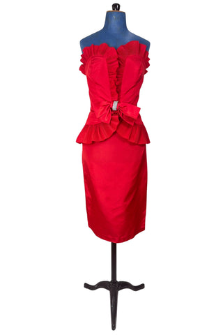 Vintage late 1980s or early 1990s cocktail dress in bold red acetate faille fabric with subtle ribbed texture. The strapless bodice has a wrapped appearance, trimmed with wide panels of accordion pleated ruffles. A large bow at the waist is crowned with a wide band of rhinestones.

Designed with an hourglass silhouette, the dress hugs and accentuates curves for a bombshell fit. 

Marked size 9/10 (vintage sizing - see measurements section at right).

Designed by Collections JS. Made in Canada.