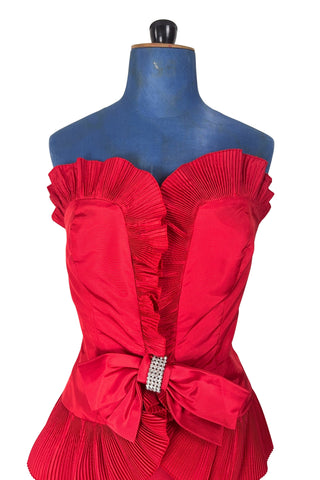 Vintage late 1980s or early 1990s cocktail dress in bold red acetate faille fabric with subtle ribbed texture. The strapless bodice has a wrapped appearance, trimmed with wide panels of accordion pleated ruffles. A large bow at the waist is crowned with a wide band of rhinestones.

Designed with an hourglass silhouette, the dress hugs and accentuates curves for a bombshell fit. 

Marked size 9/10 (vintage sizing - see measurements section at right).

Designed by Collections JS. Made in Canada.