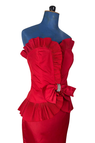 Vintage late 1980s or early 1990s cocktail dress in bold red acetate faille fabric with subtle ribbed texture. The strapless bodice has a wrapped appearance, trimmed with wide panels of accordion pleated ruffles. A large bow at the waist is crowned with a wide band of rhinestones.

Designed with an hourglass silhouette, the dress hugs and accentuates curves for a bombshell fit. 

Marked size 9/10 (vintage sizing - see measurements section at right).

Designed by Collections JS. Made in Canada.
