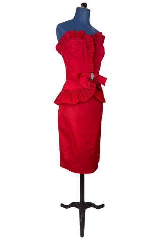 Vintage late 1980s or early 1990s cocktail dress in bold red acetate faille fabric with subtle ribbed texture. The strapless bodice has a wrapped appearance, trimmed with wide panels of accordion pleated ruffles. A large bow at the waist is crowned with a wide band of rhinestones.

Designed with an hourglass silhouette, the dress hugs and accentuates curves for a bombshell fit. 

Marked size 9/10 (vintage sizing - see measurements section at right).

Designed by Collections JS. Made in Canada.